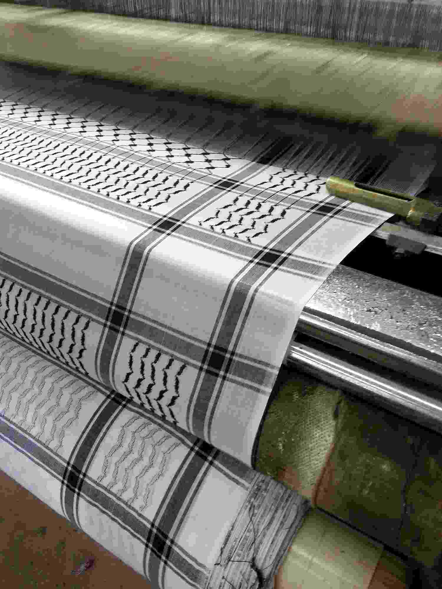 A close up of the rollers of a weaving machine creating traditional black and white ‘Keffiyeh’ scarves
